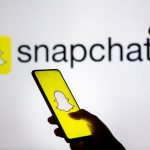 In this photo illustration, a woman's silhouette holds a smartphone with the Snapchat logo displayed on the screen and in the background.